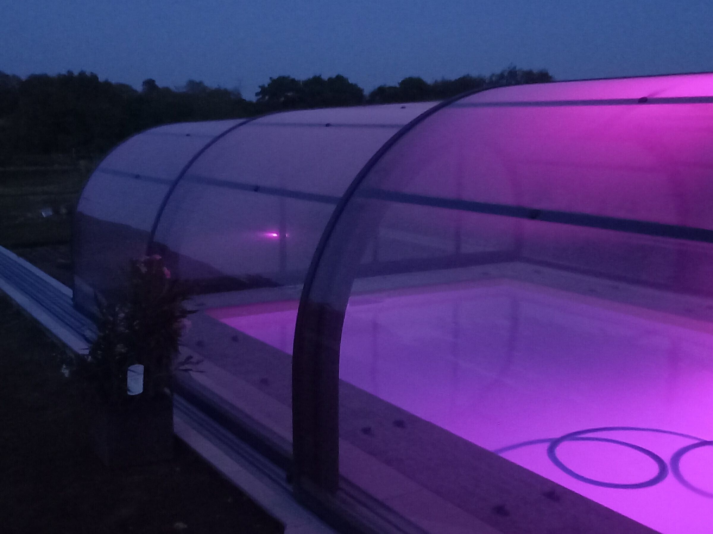 Une serre dotée d’une toiture transparente et d’un éclairage intérieur de couleur violette.