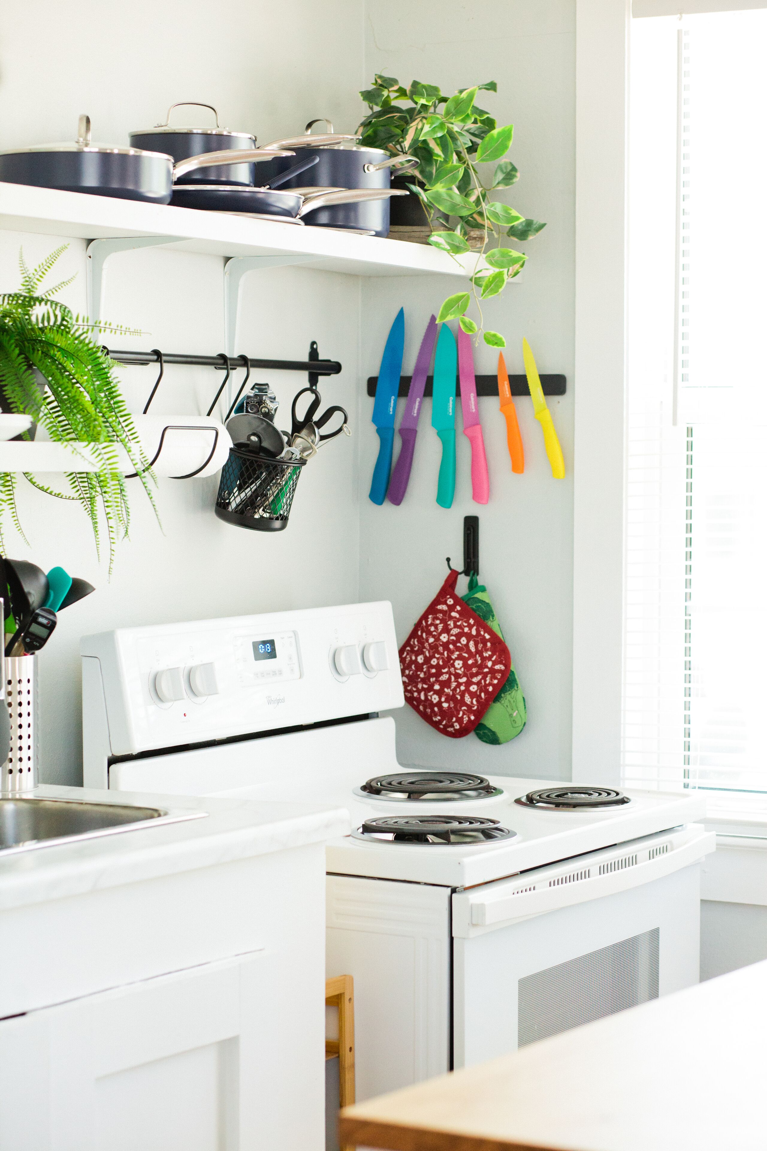A kitchen with white cabinets, a stove, and a hanging rack with kitchen utensils.