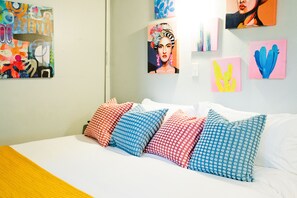 Un lit avec plusieurs oreillers, un mur blanc et plusieurs œuvres d’art.