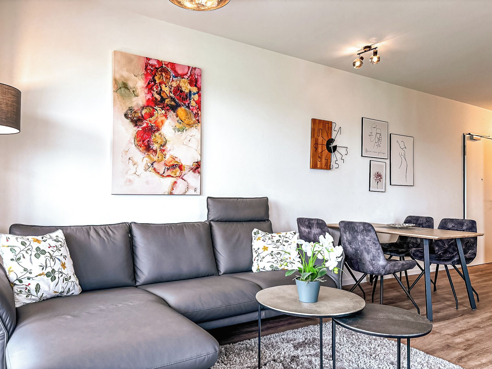 A modern living room with a grey sectional sofa, a round coffee table, and a dining area with a wooden table and chairs.