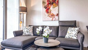 A modern living room with a grey sectional sofa, a round coffee table, and a floral-patterned pillow. - Weiße Villen Wohnung 04 (Ostseebad Boltenhagen)