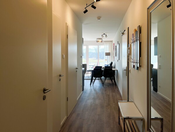 A hallway with a dining area, a bench, and a large mirror on the right.