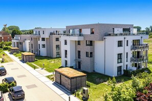 A modern residential building with multiple balconies, a paved driveway, and a well-maintained lawn.