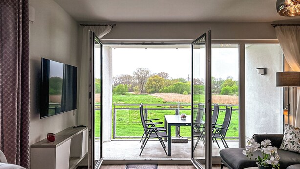 A modern living room with a TV, sofa, and a balcony with a table and chairs. - Weiße Villen Wohnung 04 (Ostseebad Boltenhagen)