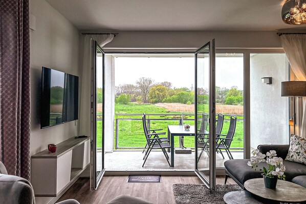 A modern living room with a TV, sofa, and a balcony with a table and chairs.