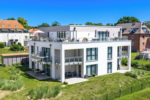 A modern two-story residential building with a flat roof, large windows, and a balcony.