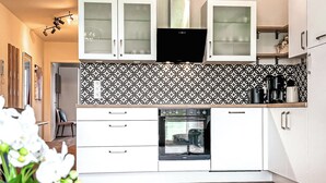 A modern kitchen with white cabinets, a patterned backsplash, and a built-in oven. - Weiße Villen Wohnung 07 (Ostseebad Boltenhagen)