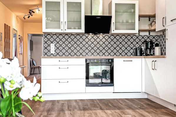 Una cocina moderna con armarios blancos, salpicadero con diseño y horno empotrado.