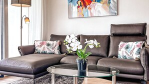 A modern living room with a brown leather sofa, a glass coffee table, and a potted orchid plant. - Weiße Villen Wohnung 07 (Ostseebad Boltenhagen)