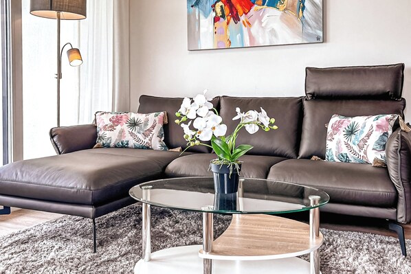 A modern living room with a brown leather sofa, a glass coffee table, and a potted orchid plant. - Weiße Villen Wohnung 07 (Ostseebad Boltenhagen)