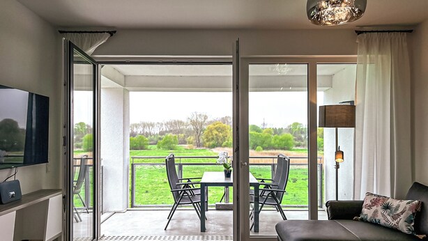 A modern living room with a sofa, a TV, and a dining area with chairs and a table. - Weiße Villen Wohnung 07 (Ostseebad Boltenhagen)