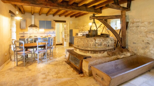Une cuisine rustique avec un mur en pierre, des poutres en bois et un moulin à pierre traditionnel.