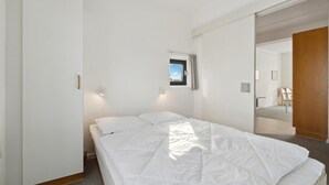 Een slaapkamer met een bed, een klein raam en een deur naar een andere kamer.