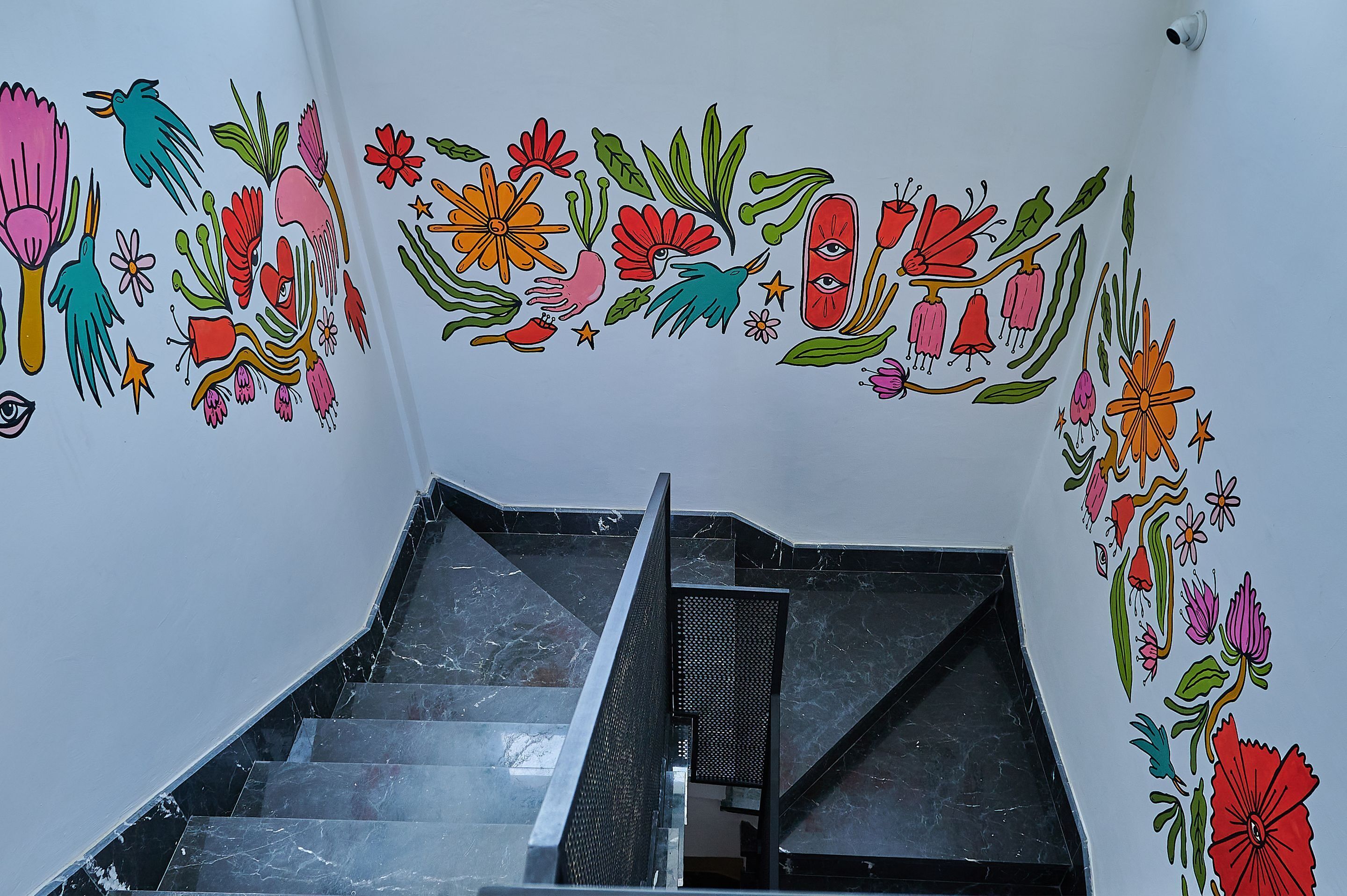 A staircase with a handrail and a wall decorated with colorful floral and bird illustrations.