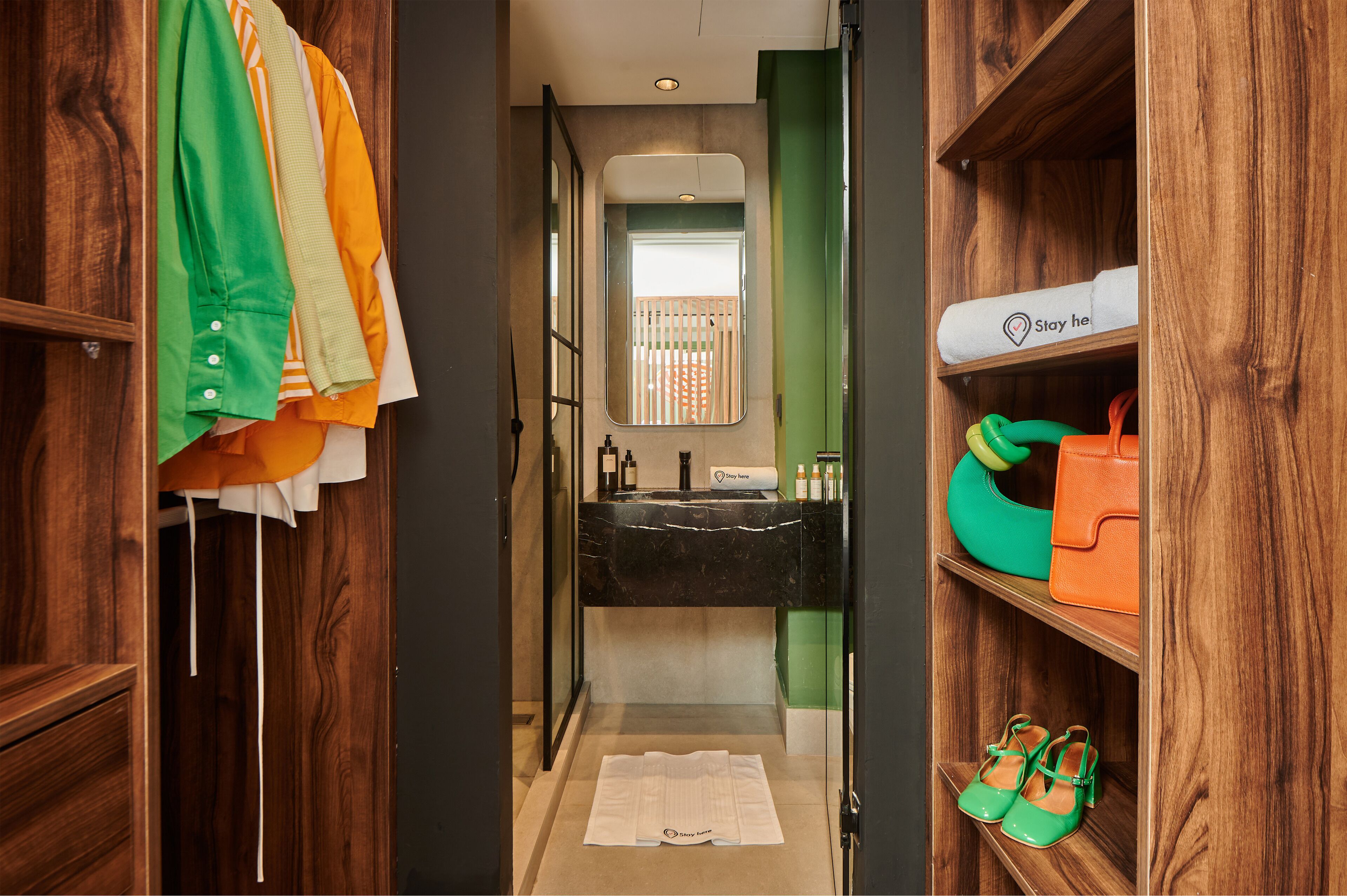 Habitación de hotel con armario de madera, espejo, lavamanos y toalla verde.