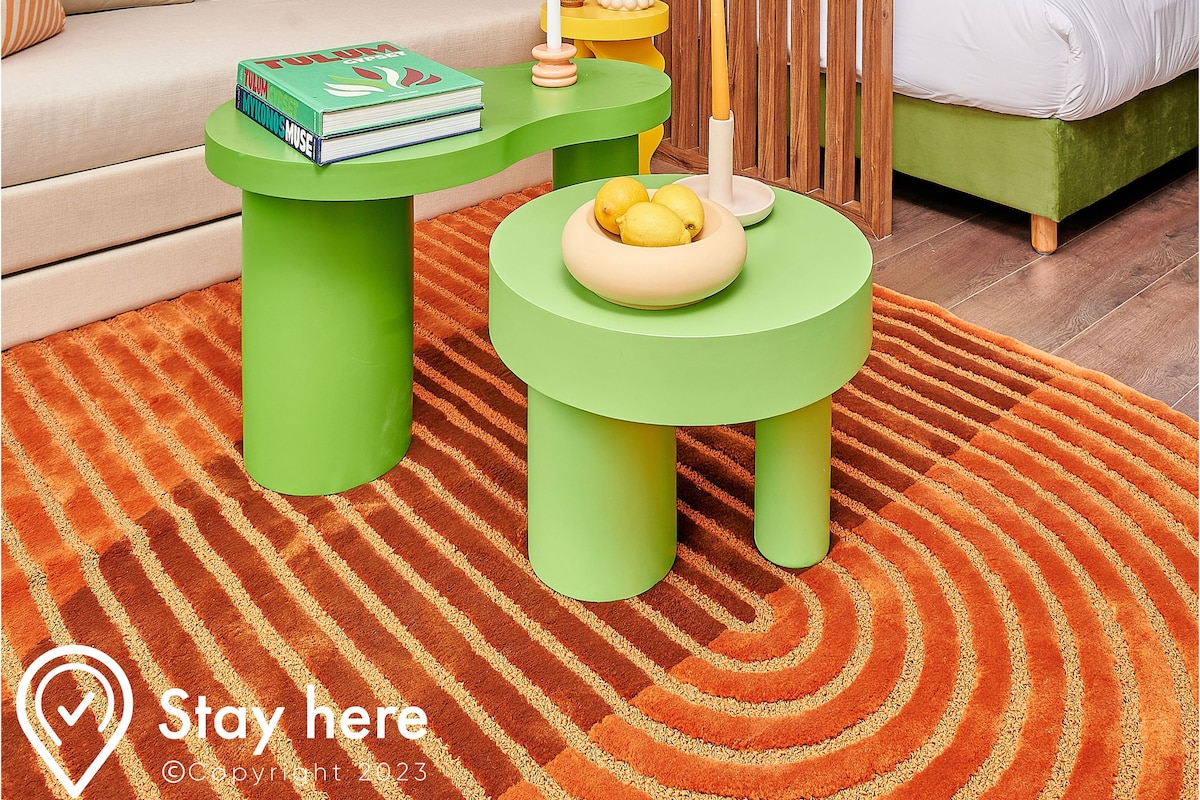 A modern living room with a sofa, two green coffee tables, a wooden partition, and a bed.
