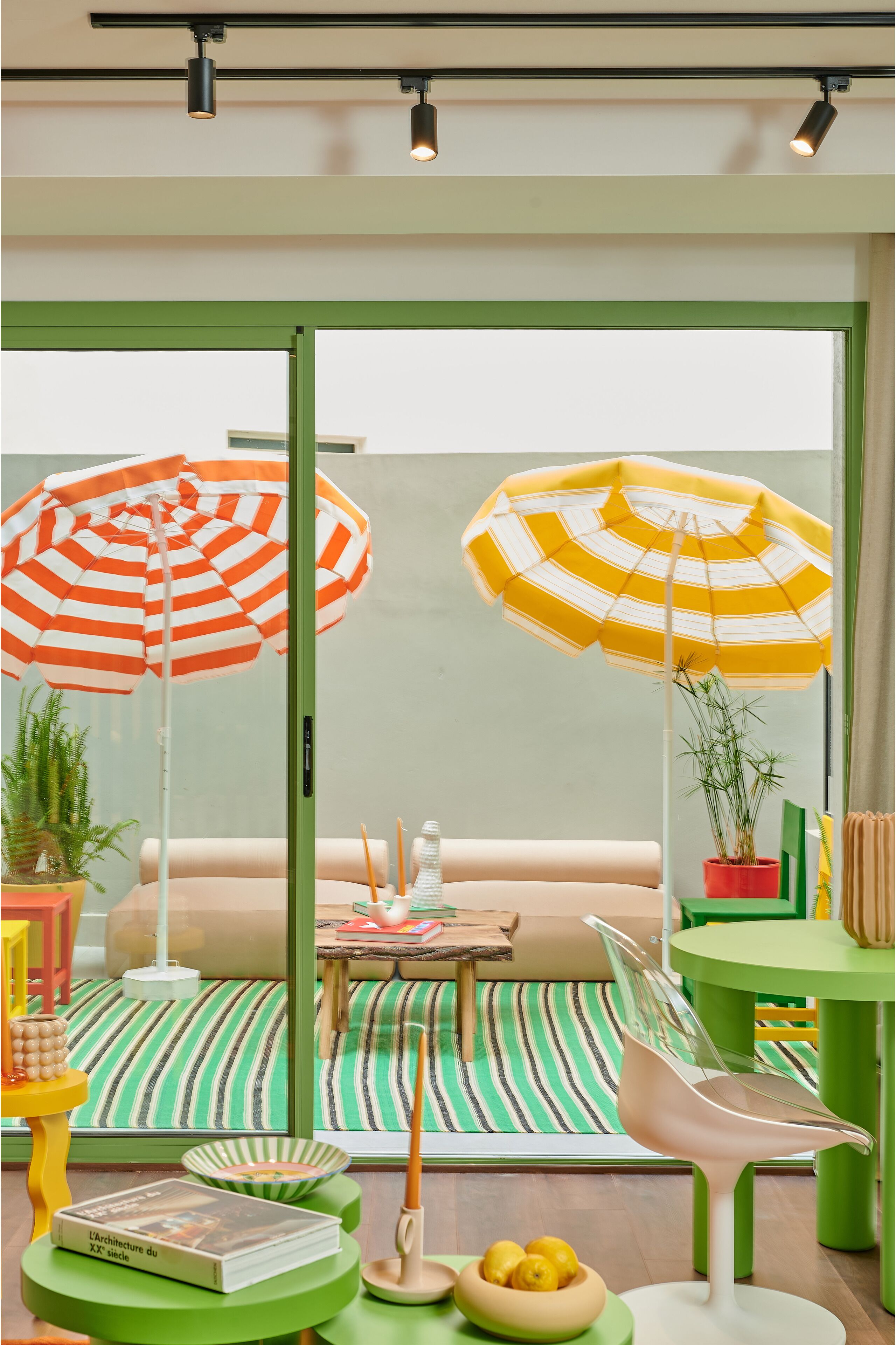 A modern interior with a green-striped floor, a seating area with a table, and two large striped umbrellas.
