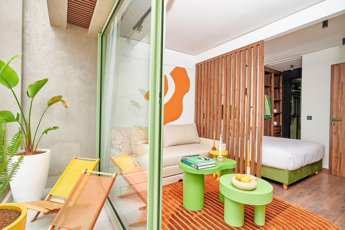 Un dormitorio moderno con una cama, un sofá, una mesa de centro verde y una planta en maceta.