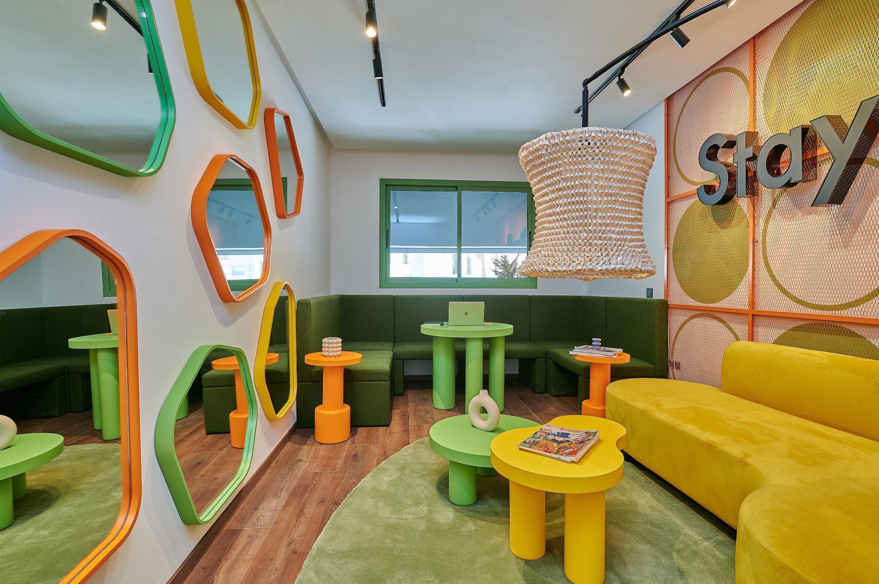 A vibrant lounge area with green and yellow furniture, a large yellow sofa, and a 'Stay' sign on the wall.