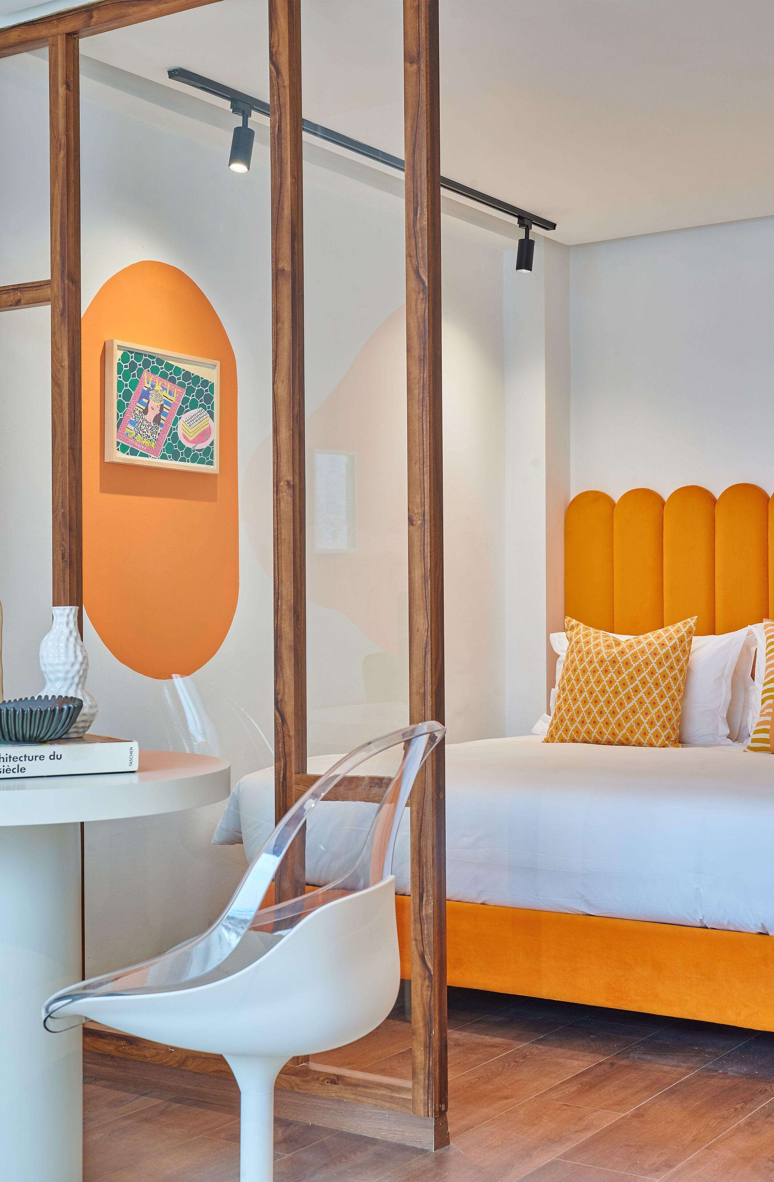 Une chambre à coucher moderne avec une tête de lit en bois, une chaise blanche et une petite table sur laquelle se trouvent un livre et un vase.