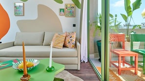 Un salón moderno con un sofá, almohadas, un cuenco y una vela. Hay un ventanal de vidrio que da a un espacio exterior con una silla y una mesa.