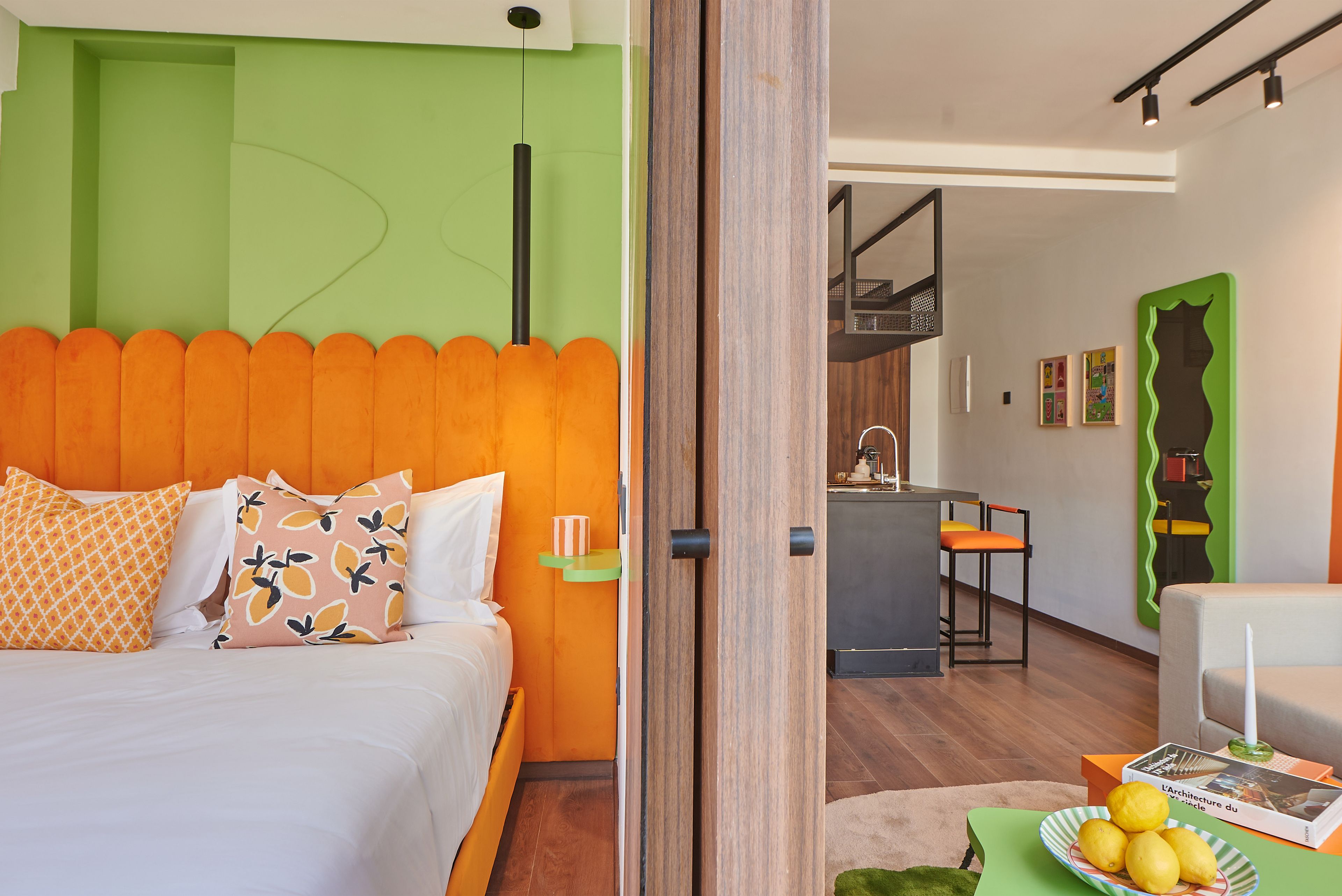Un dormitorio moderno con un cabecero de color naranja brillante, una cama con almohadas blancas y estampadas, y una pared de acento verde.