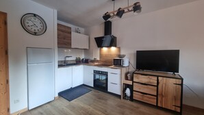 A compact kitchen with a built-in oven, microwave, and sink. There's a clock on the wall and a small dog in the corner. - Bel Appartement Avec Piscine - Le Grand Tétras (Samoëns)