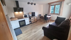 A compact kitchen with modern appliances, a dining area with a table and chairs, and a dark-colored sofa in a living area. - Bel Appartement Avec Piscine - Le Grand Tétras (Samoëns)
