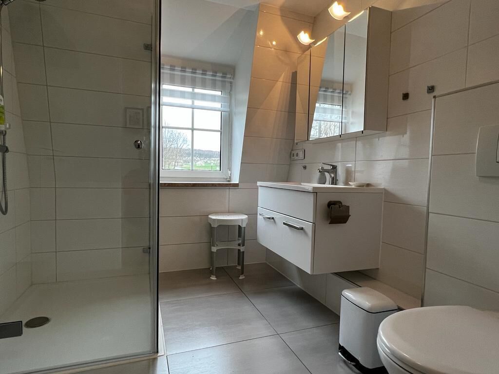 A modern bathroom with a glass-enclosed shower, a white toilet, a vanity with drawers, and a window with blinds.