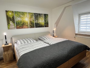 A bedroom with a bed, two bedside tables, and a window with blinds. - Ferienwohnung im Grünen in Osterwieck am Fallstein (Osterwieck)