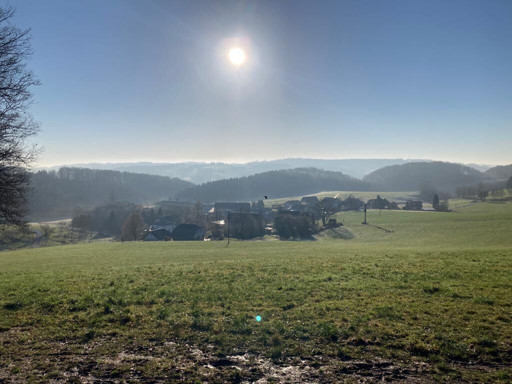 A rural landscape with a clear sky, a sunlit field, and a distant village.