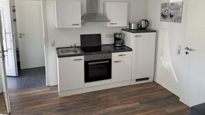 A compact kitchen with white cabinets, a stove, oven, and a coffee maker. - Büschem feel-good paradise (Lindlar)