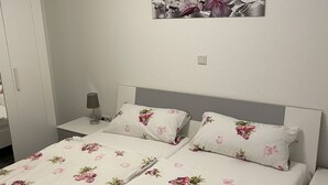 A neatly made bed with floral bedding, a bedside table with a lamp, and a wall-mounted picture of flowers. - Büschem feel-good paradise (Lindlar)