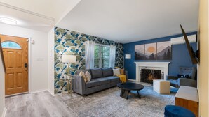 Ein Wohnzimmer mit grauem Sofa, blauem Sessel, Kamin und Wandpapier mit Muster.