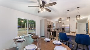 Ein moderner Essbereich mit einem großen Holztisch, gedeckt für sechs Personen, einem Deckenventilator und Blick auf den Garten.