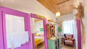 A room with a purple door, a bed with a yellow bedspread, a small wooden cabinet, and a chair with a patterned cushion. - Mell10 House (Urla)