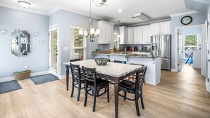Une cuisine moderne avec des meubles blancs, des appareils en acier inoxydable et un coin repas comprenant une table et des chaises en bois.