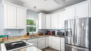 Une cuisine moderne avec des meubles blancs, des appareils en acier inoxydable, des comptoirs en granit et une fenêtre donnant sur un paysage verdoyant.