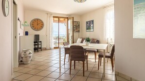 A dining area with a table and chairs, a large wall clock, and a view through a glass door. - Lago Blu with pool and lake view (Manerba del Garda)