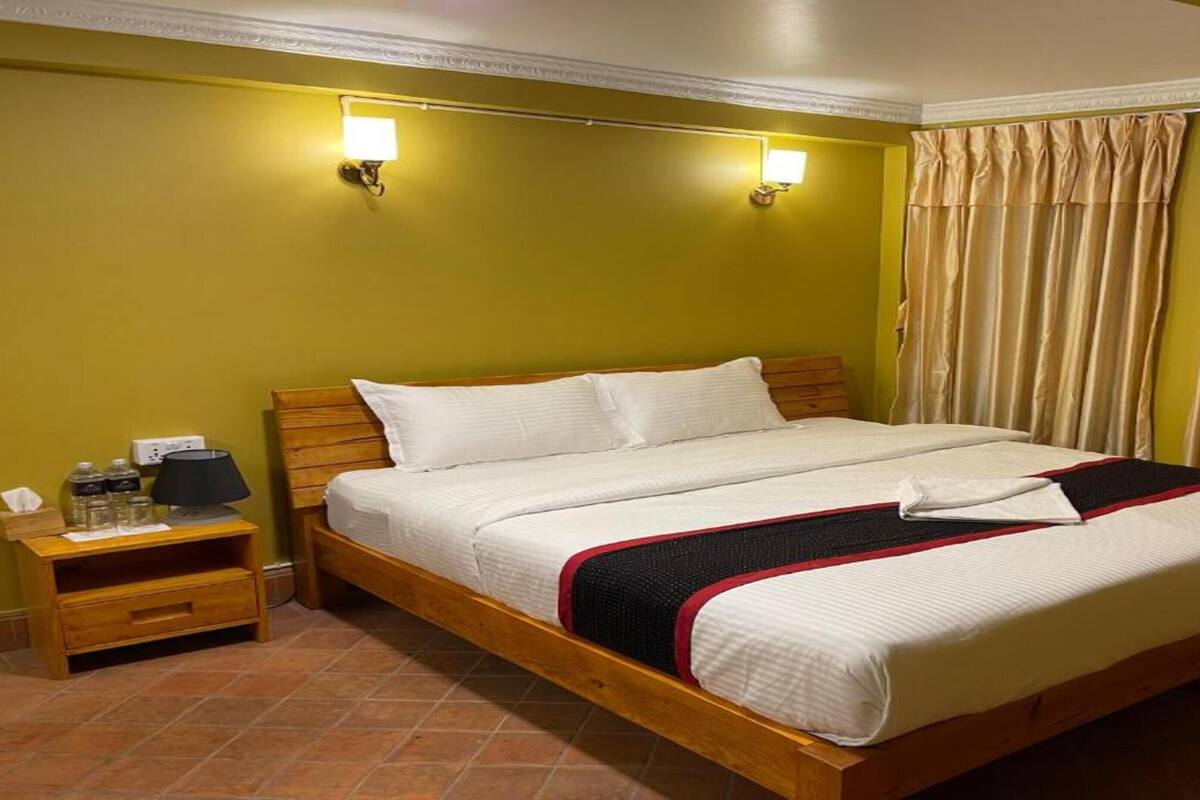 Habitación de hotel con una cama grande, dos lámparas de noche, una mesita de noche y una cortina.