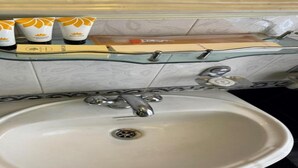 A bathroom with a glass shelf holding toiletries, a sink with a drain, and a mirror above the sink. - MeroStay 149 HE (Bhaktapur)