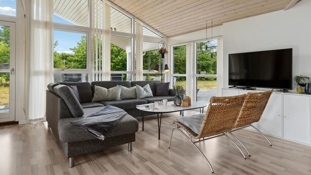 A modern living room with a grey sofa, a coffee table, and a wicker chair. A flat-screen TV is mounted on the wall. - Gorgeous home in Fjerritslev with sauna (Fjerritslev)