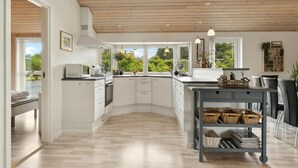 A modern kitchen with white cabinetry, a central island, and a view of greenery outside. - Gorgeous home in Fjerritslev with sauna (Fjerritslev)
