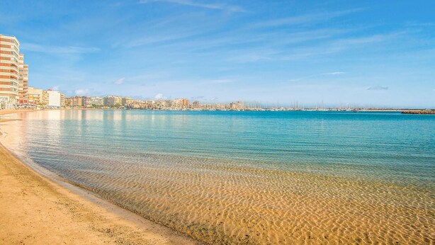 Paisatge costaner amb mar blau clara, platja de sorra i una filera d'edificis al costat de la platja.