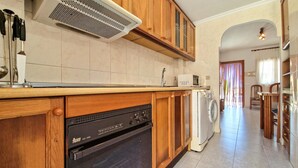 Una cuina amb armaris de fusta, forn integrat, rentadora i microones.