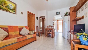Un saló amb un sofà, cadires, una taula de dinar i una televisió. Hi ha portes que condueixen a altres espais.