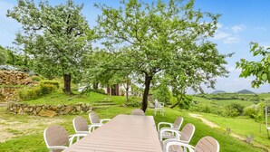 Un área de comedor al aire libre con una mesa larga y sillas, rodeada de abundante vegetación y árboles.
