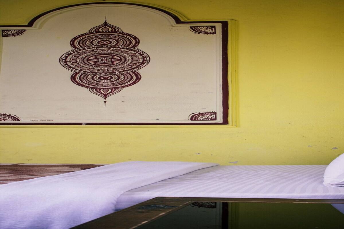 A single bed with a white mattress and pillow, a small bedside table with a tissue box, and a wall with a decorative pattern.