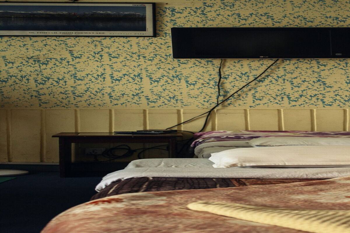 A bedroom with two beds, a television mounted on the wall, and a small table with a lamp.