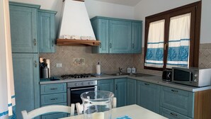 A kitchen with teal cabinets, a stove, oven, microwave, and a window with curtains. - Villa Crilu Sardinia, cozy, with sea view, swimming pool and private parking space (Tanaunella)
